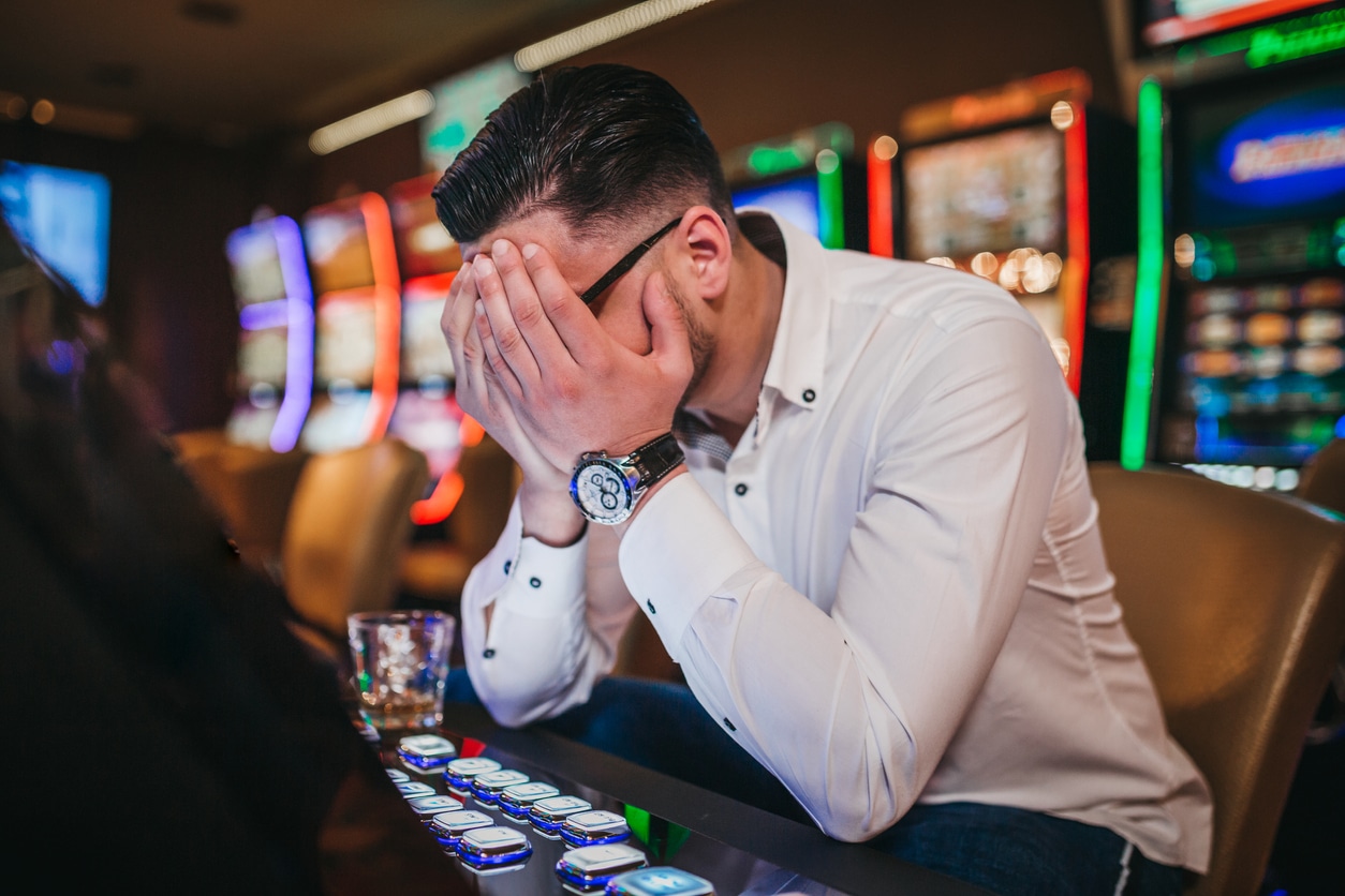 Gambling addict holding his hands in his face sitting at a table with a glass of alcohol