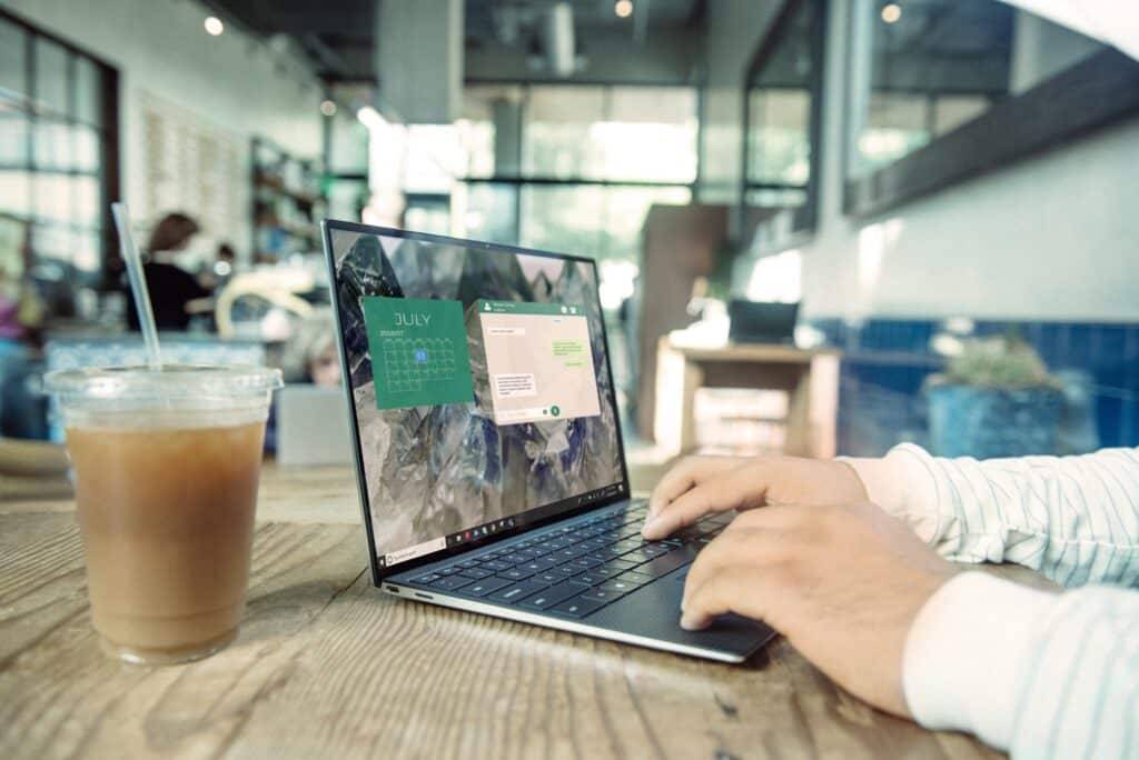 Two hands working on a laptop with a drink next to it