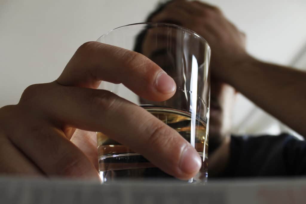 Alcoholic man with his hand pressed against his head while holding a glass of liquor