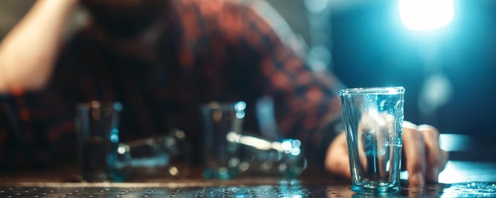 Alcoholic man sitting at a bar with empty shot glasses in front of him