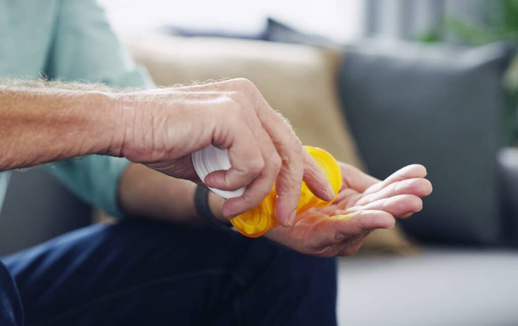 Older man struggling with drug addiction pouring prescription pills into his hand