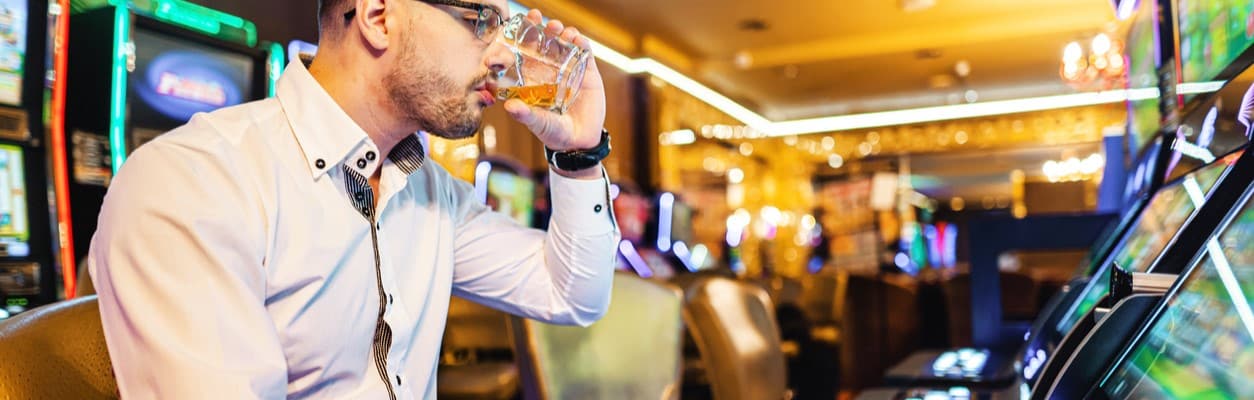Man sitting a slot machine drinking a glass of hard liquor