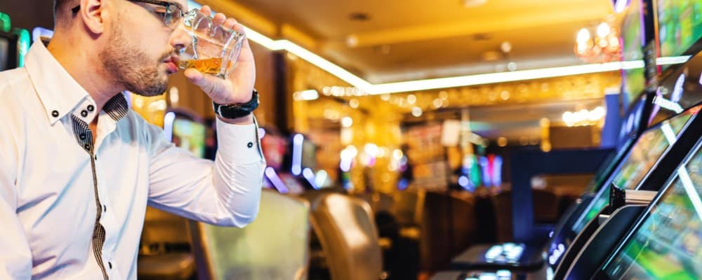 Man sitting a slot machine drinking a glass of hard liquor