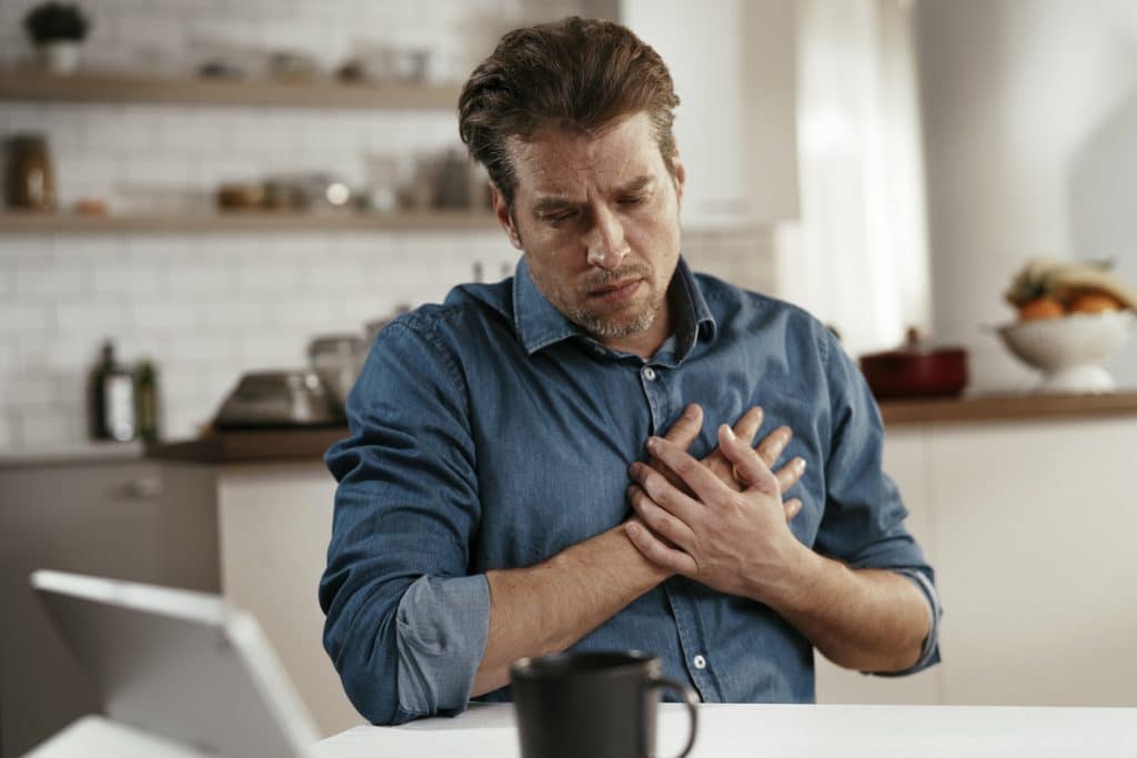 Man with adderall addiction experiencing chest paid while sitting at a table with his laptop