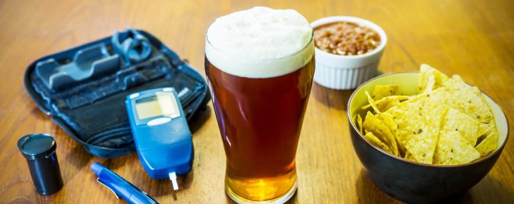 A glass of beer with chips and salsa next to a diabetes test kit