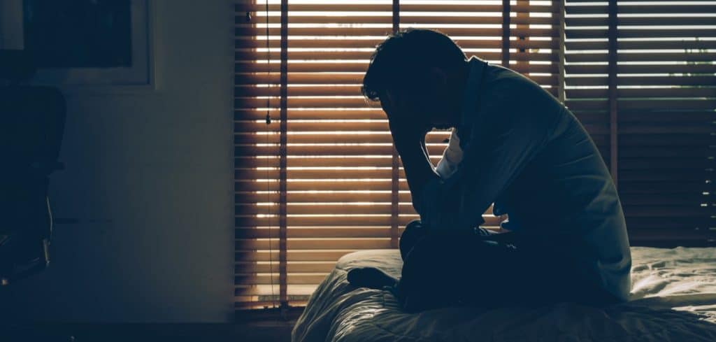Depressed man with a gambling addiction sitting on his bed after getting home at sunrise